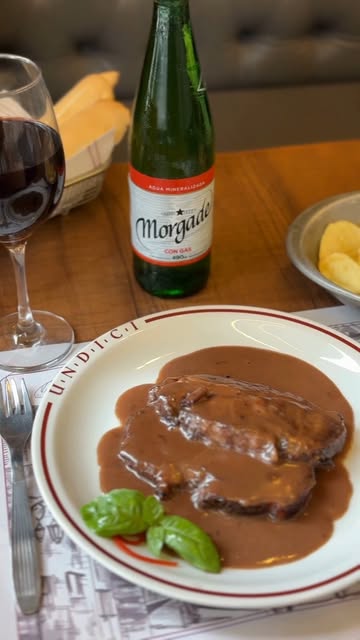 Osobuco con salsa, copa de vino tinto y botella de agua mineralizada